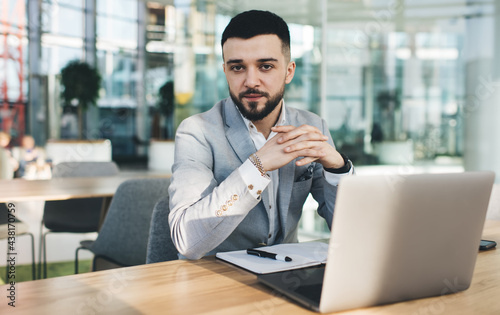 Young confident businessman at desk with open notebook and laptop