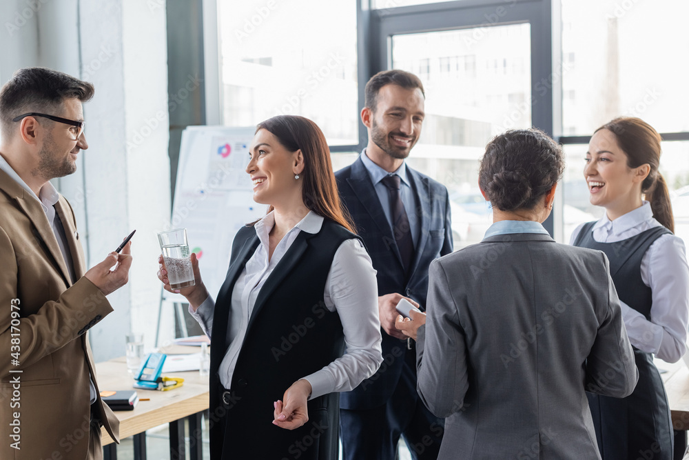 Positive multicultural business people with smartphone and water talking in office