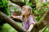 Little preschool girl climbing on tree on family backyard. Lovely happy toddler child hanging on magnolia tree, active games with children outdoors. Outdoor activity in park or garden