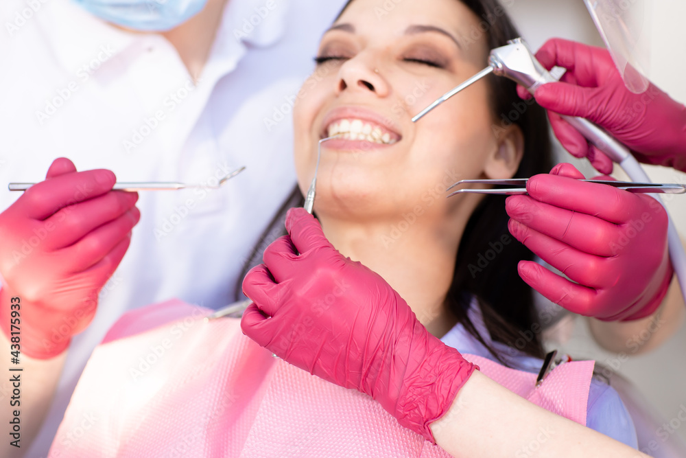 Close up hands of two dentists in pink gloves with tools and smiling young woman in a dental chair on the background. Healthy and white smile, dentistry concept Close up hands of two dentists in pink gloves with tools and smiling young woman in a dental chair on the background. Healthy and white smile, dentistry concept