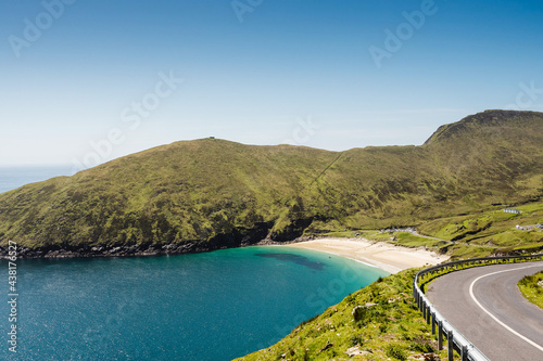Small narrow road to Keem beach, Achill island in county Mayo, Ireland, warm sunny day. Clear blue sky and water of the Atlantic ocean.