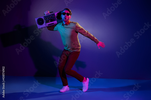Full size photo of young funny guy dance with boom box wear eyewear sweater pants isolated on blue color background