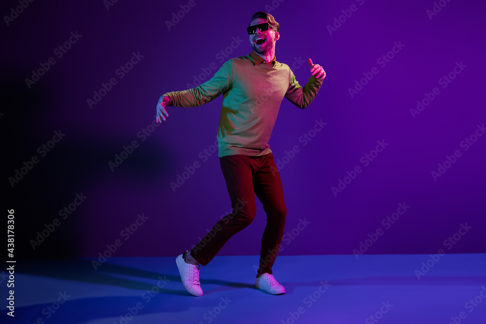 Full length photo of cheerful positive young man look empty space dance disco wear sunglass isolated on neon background