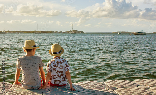 Two kids sitting on a plastic dock at waterfront. Family vacation concept, friendship. Copy space for your text