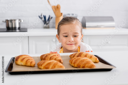 Happy kid looking at blurred croissants on baking sheet