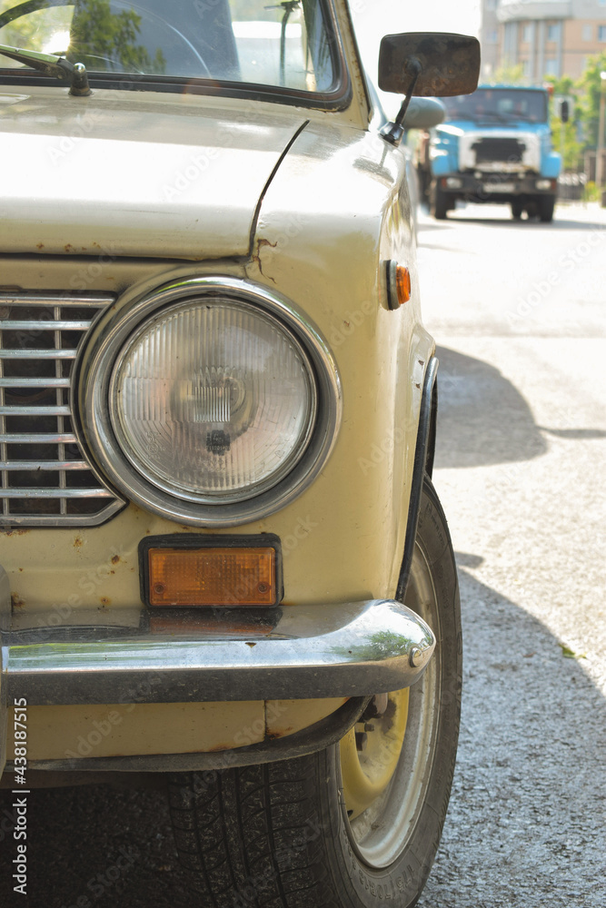 round headlight of a vintage old Russian rusty car in beige color close-up.