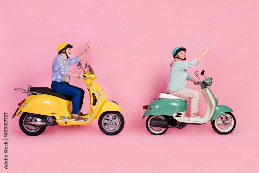 Full size profile side photo of happy mature stylish male female ride moped phone selfie show v-sign isolated on pink color background