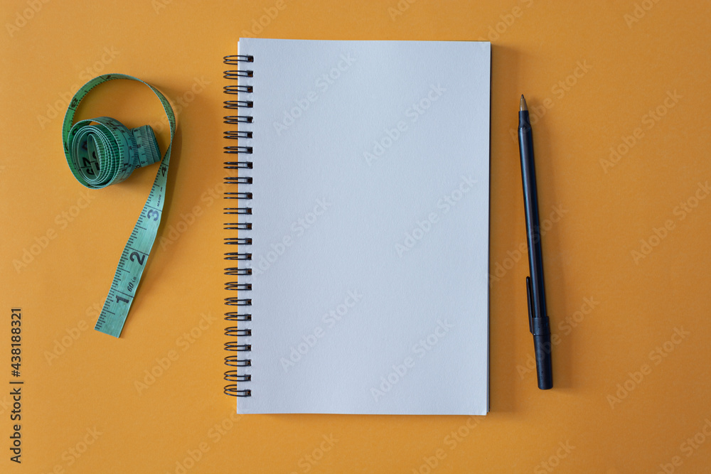 Notepad with pen and measurement tap on yellow background Notepad with pen and measurement tap on yellow background