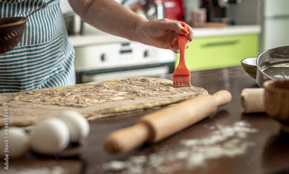 Obraz premium Woman is sprinkling cinnamon on raw dough to make fragrant homemade buns. Concept of the cooking process of baking