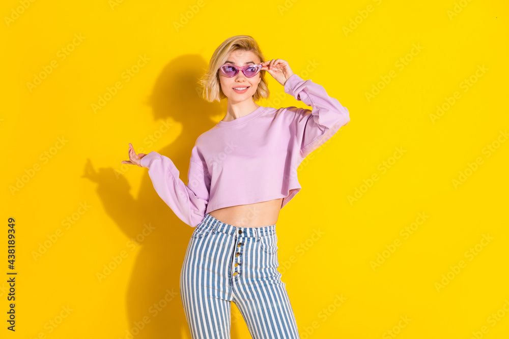 Photo of young girl happy positive smile hand touch sunglass look empty space isolated over yellow color background Photo of young girl happy positive smile hand touch sunglass look empty space isolated over yellow color background