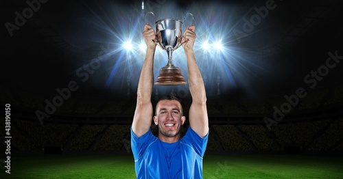 Portrait of caucasian male athlete lifting a trophy against floodlights in background