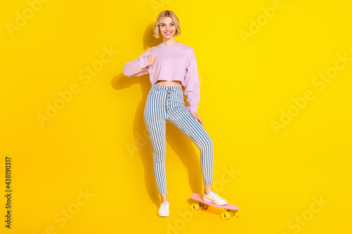 Full length photo of happy nice young woman make thumb-up stand skateboard isolated on yellow color background