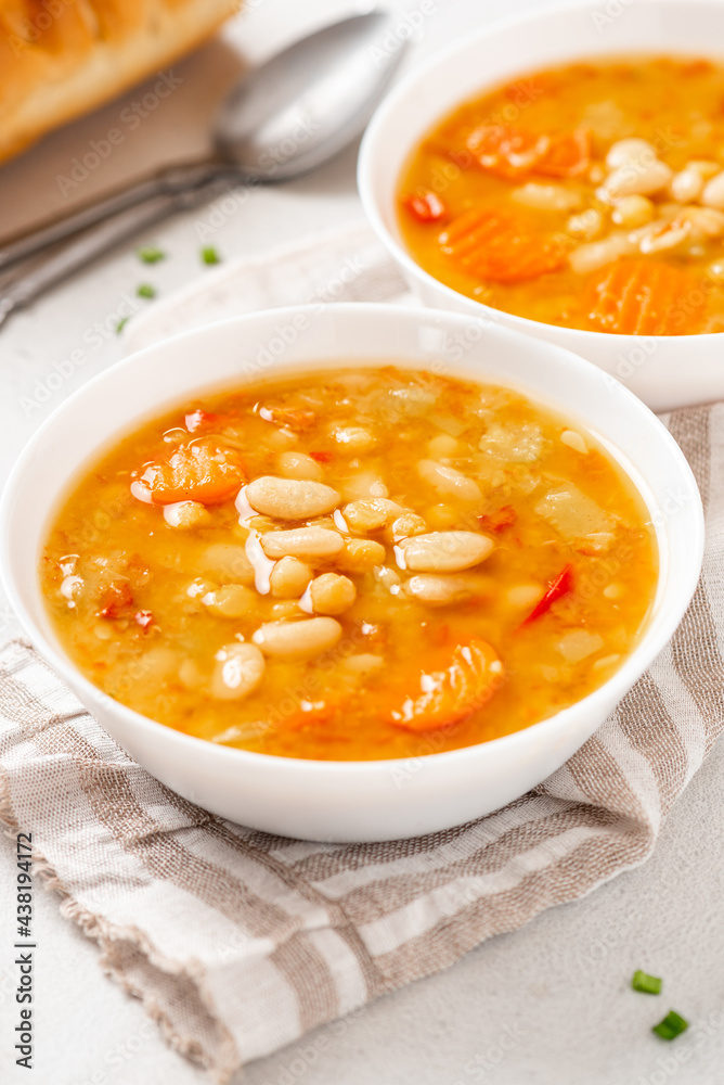 Soup with beans and vegetables in a white bowl on a gray concrete background closeup. Soup made from lentils, chickpeas, white beans, carrots, peppers, and tomatoes. Tasty vegan soup, vegetarian food. Soup with beans and vegetables in a white bowl on a gray concrete background closeup. Soup made from lentils, chickpeas, white beans, carrots, peppers, and tomatoes. Tasty vegan soup, vegetarian food.