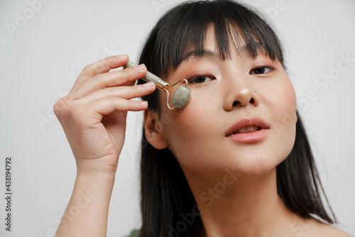 Young asian woman with piercing massaging face with jade roller