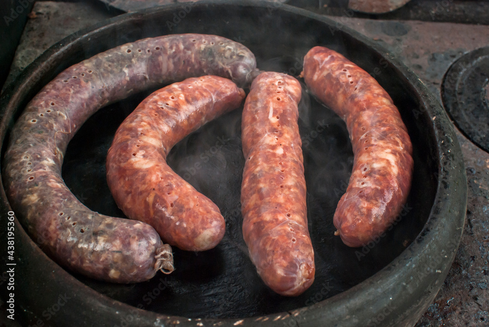 Roasted sausages prepared in earthen clay pot on rural outside oven
