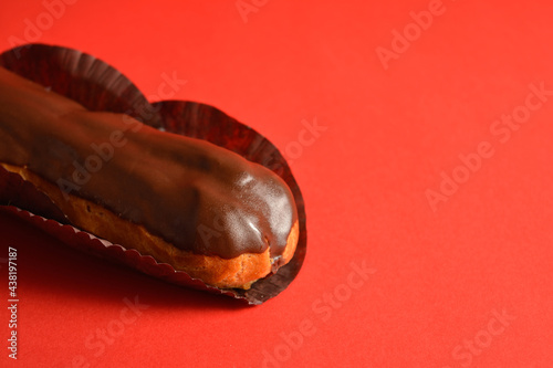 Close up to part of French dessert on red background. Eclair with custard filling and dark chocolate on top. Copy space image creative concept. Sweet menu object 