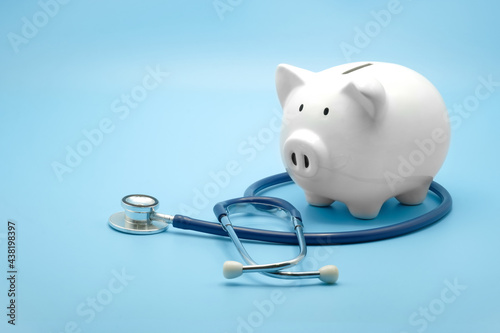 Piggy bank with stethoscope isolated on light blue background with copy space. Health care financial checkup or saving for medical insurance costs concept.
