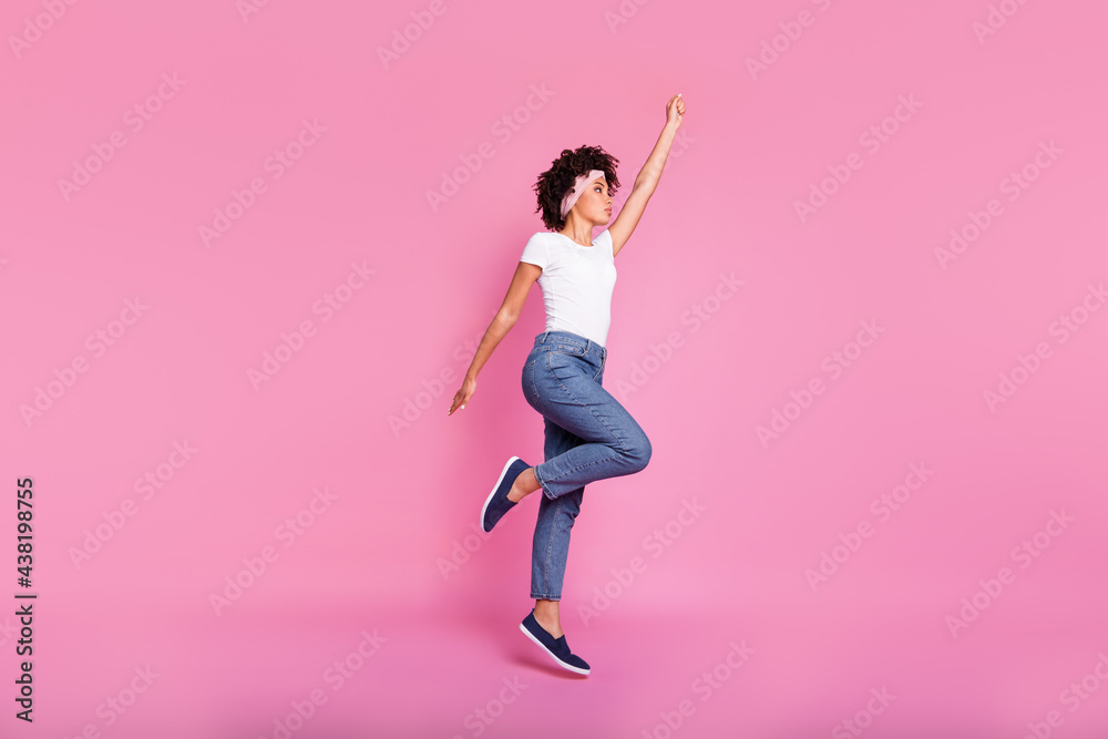 Full length body size photo of pretty girl wearing jeans jumping like super woman isolated pastel pink background
