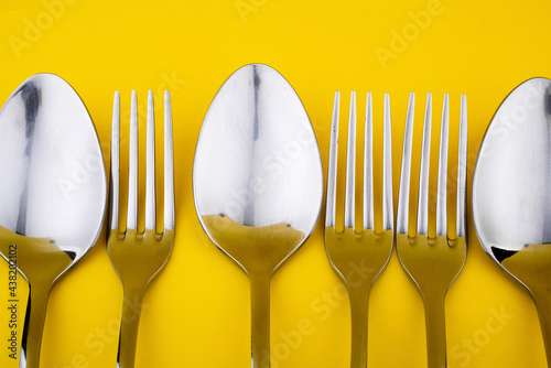 Close-up and selective focus of the set of dinning cutlery on a yellow background. Flat lay and top view of a spoon, fork, and knife with copy space. Kitchen equipment for food.