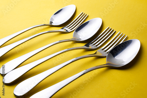 Close-up and selective focus of the set of dinning cutlery on a yellow background. Flat lay and top view of a spoon, fork, and knife with copy space. Kitchen equipment for food.
