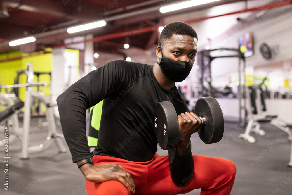 Concentrated young black male athlete exercising with dumbbell in gym