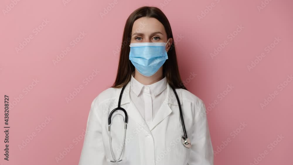 Young female doctor in medical uniform and facemask against coronavirus pandemics. Woman GP or physician in facial mask from covid-19 epidemics, isolated on pink studio background. Coronavirus concept Young female doctor in medical uniform and facemask against coronavirus pandemics. Woman GP or physician in facial mask from covid-19 epidemics, isolated on pink studio background. Coronavirus concept