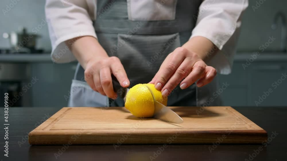 Female hands cut lemon in half by kitchen knife in the kitchen 
