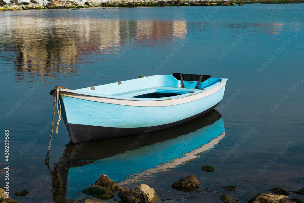 Una piccola imbarcazione azzurra ormeggiata con alcuni riflessi nell'acqua del mare.