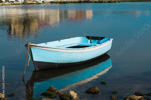 Una piccola imbarcazione azzurra ormeggiata con alcuni riflessi nell'acqua del mare.