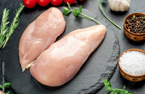 Raw chicken breasts with spices on a stone background