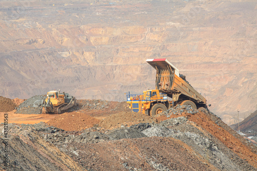 Large open-pit truck and bulldozer work at the waste rock dump near the ore pit