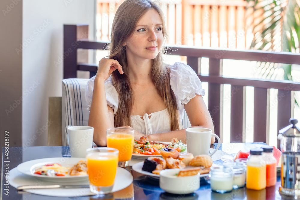 Young Smiling Woman Sitting on Breakfast with Plates Full of Food - Fresh Omelette, Vegetables, Fruits and Orange Juice in Glass. Morning Food in Luxury Hotel