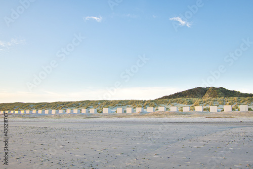 Horizontal view on a beach with a row of beach cabins at sunset in spring. North sea beach with dunes in Zeeland on a sunny day. Copy space.