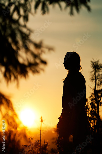 A girl in silhouette in sun set in the forest. Summer days. It is hot and warm. Two sisters are playing in the woods. Golden hour with strong and bright sunlight.