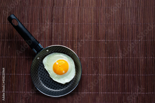Frying pan with fried egg on a bamboo table