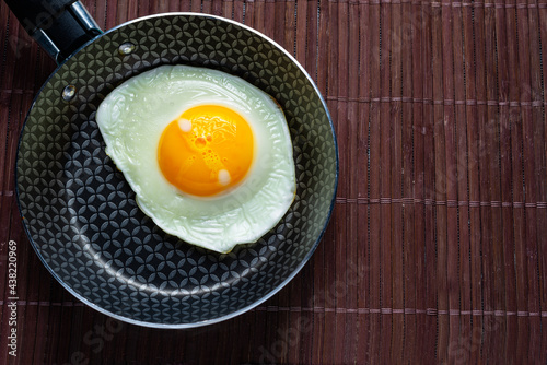 Frying pan with fried egg on a bamboo table