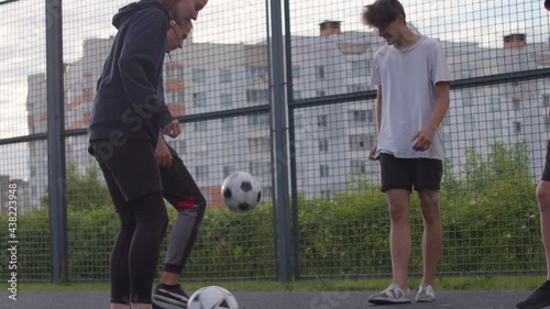 Close up of young happy smiling amateur football players perform tricks with the soccer ball before to start a friendly match or training workout game on court in a sunny day. 4K RAW graded footage photo