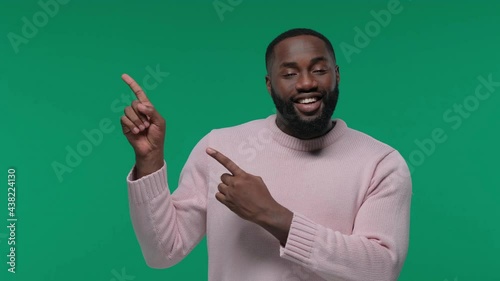 happy young man pointing finger showing to copy space over green background in the studio