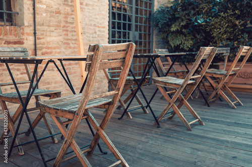 Wooden chairs and tables, empty, in the outdoor dehors area of a little bar or restaurant in a medieval touristic burg in Italy. Mid afternoon, no one around.