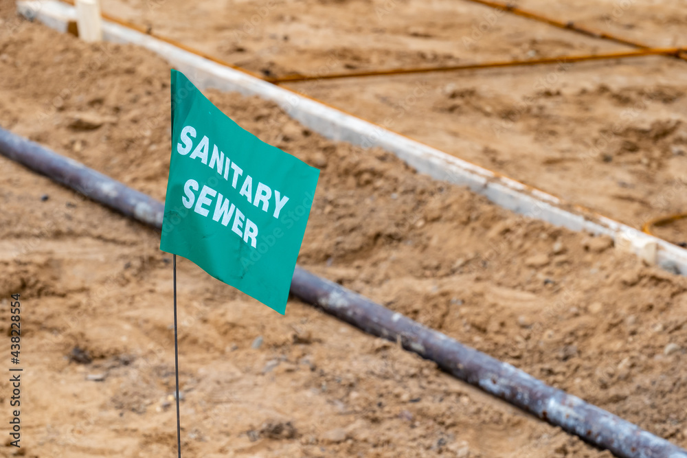 Small green flag with white lettering, warning of an underground sanitary sewer line, at a new home construction site.