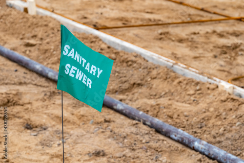Obraz na płótnie Small green flag with white lettering, warning of an underground sanitary sewer line, at a new home construction site. w salonie