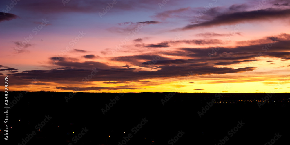 Fiery yellow underscores this beautiful pink and purple sunrise panorama illuminating the sky behind dark clouds over the city of Colorado Springs, El Paso County, Colorado.