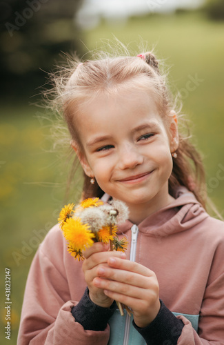 Portrait of a beautiful girl with flowers in her hands in the park in the summer. The girl loves to spend time alone. Vertical