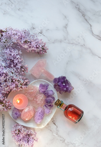 gemstones minerals, essential oil bottle, candle, lilac flowers on marble background. Crystal ritual, spiritual practice, body care. top view