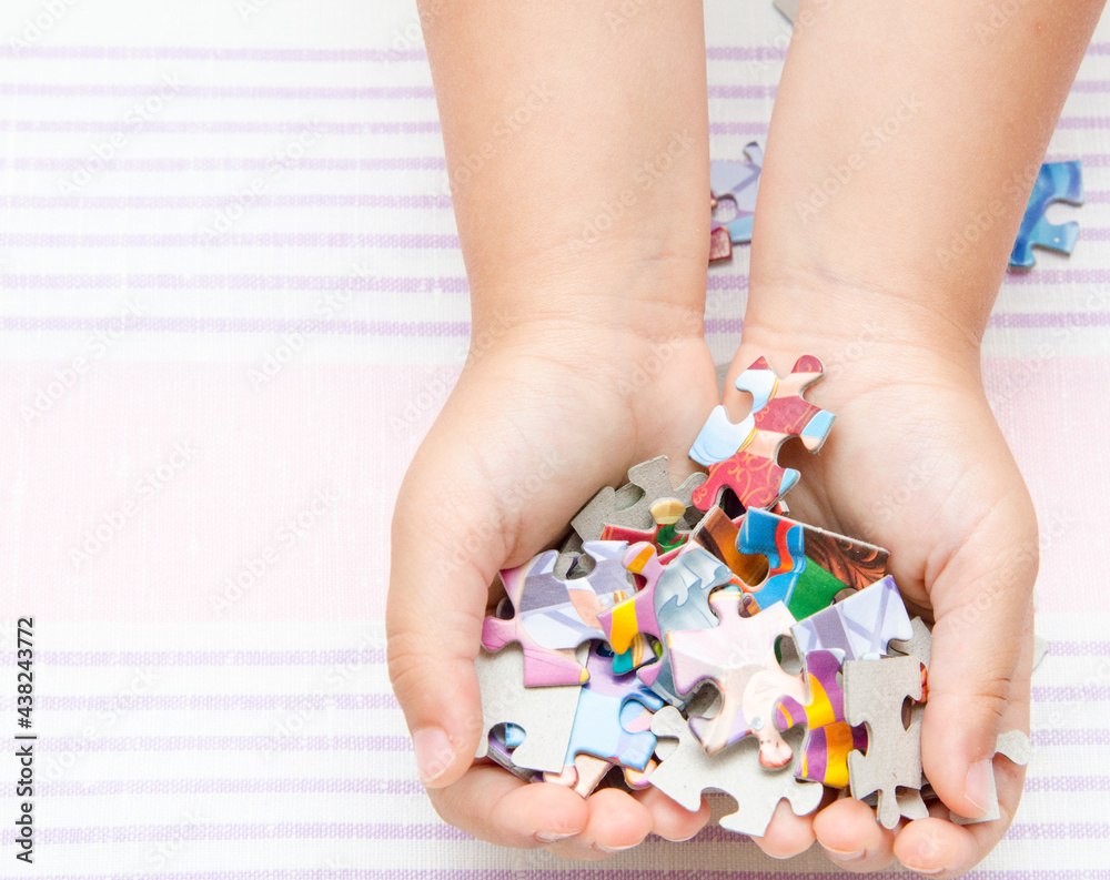The child holds the details of a colored puzzle. Pieces of the puzzle in the hands of a child. The child holds the details of a colored puzzle. Pieces of the puzzle in the hands of a child.