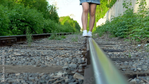 Close-up shot of a girl walking on the rails. Walk along the railroad tracks. Old train track © Sergei Puzankov