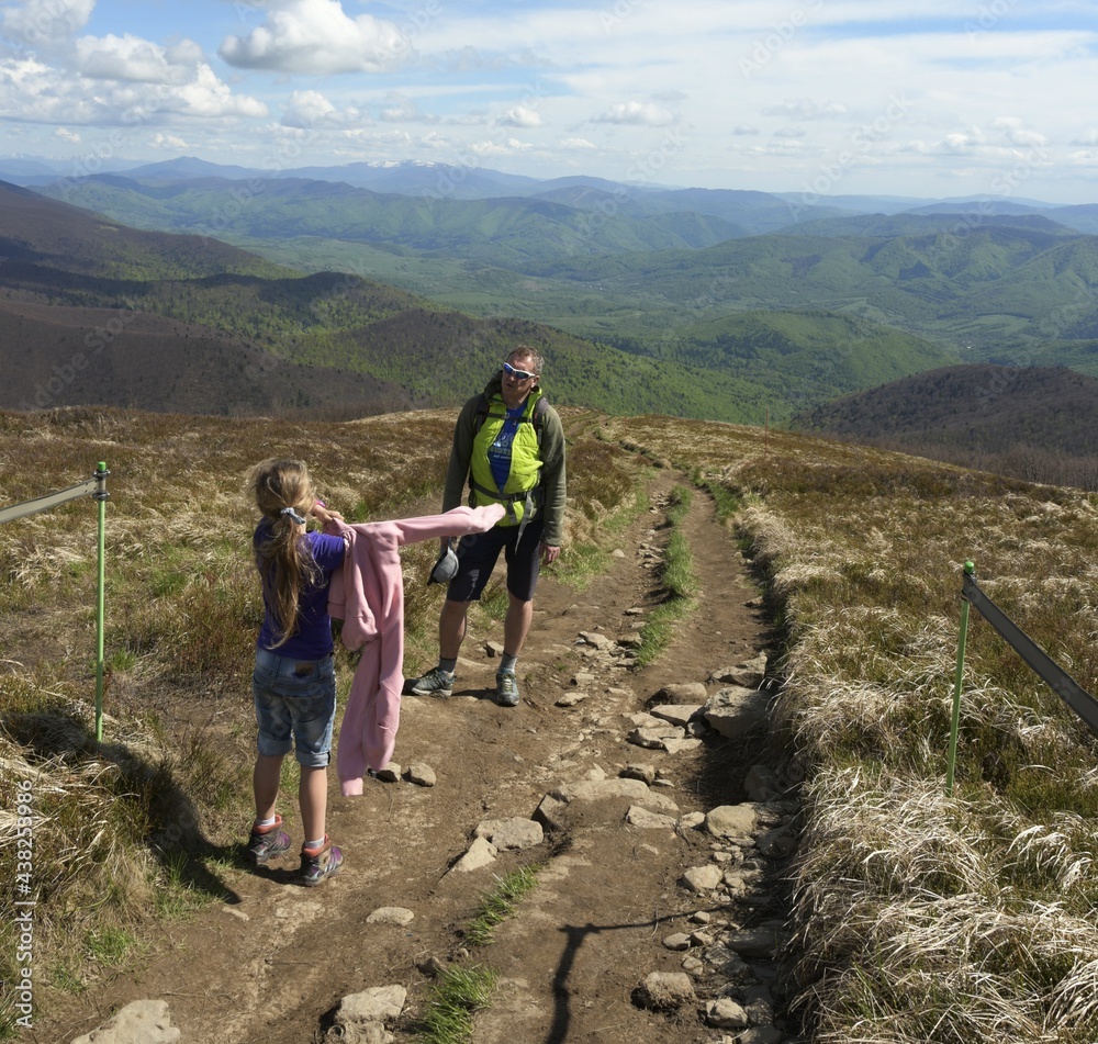 Spring trip to the Bieszczady mountains with a kid. A girl against the backdrop of the mountains is getting dressed.
