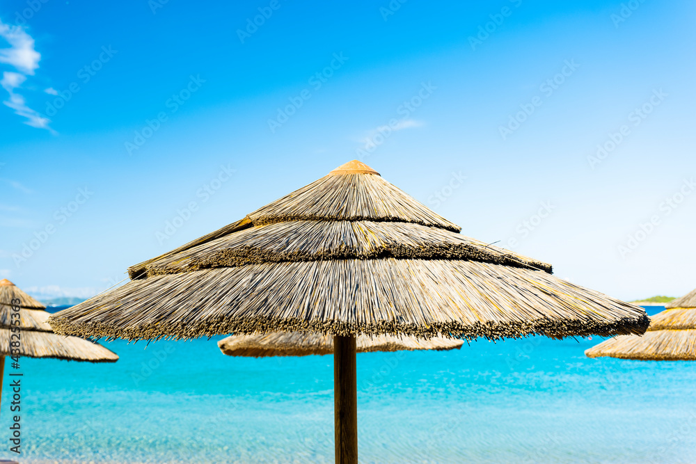 (Selective focus) Stunning view of a thatch umbrella in the foreground and beautiful turquoise sea in the background. Romazzino Beach, Porto Cervo, Sardinia, Italy.