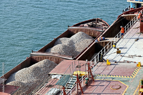 Loading bulk cargo of limestone from barges into a bulk carrier by using ship cranes and grabs at the port of Campha, Vietnam. October,2020. 