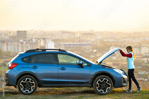 Fotografie Young woman opening bonnet of broken down car having trouble with her vehicle
